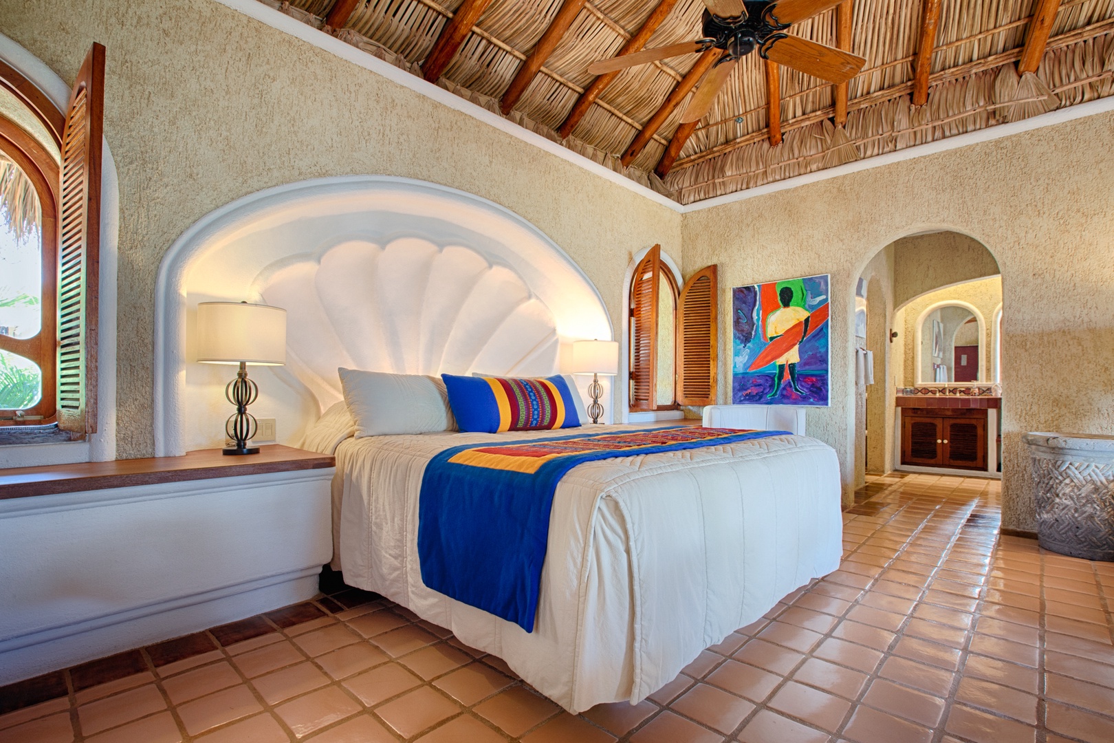 Escape to your tropical sanctuary with authentic thatched ceiling, vibrant artwork, and unique shell-inspired headboard creating an unforgettable Mexican coastal retreat.