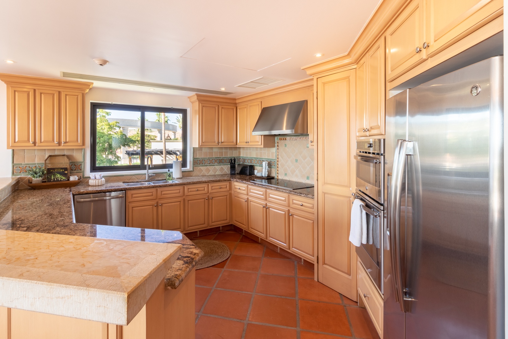 A sunlit, well-appointed kitchen awaits with gleaming stainless appliances, granite counters, and a welcoming window view—perfect for preparing your favorite meals during your stay.