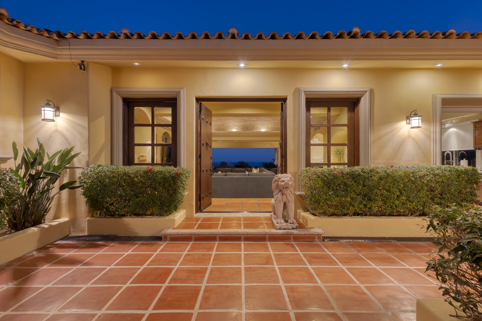 Mediterranean villa entrance featuring warm terracotta tiles, elegant lighting, and decorative stone lion statue welcoming arrivals.