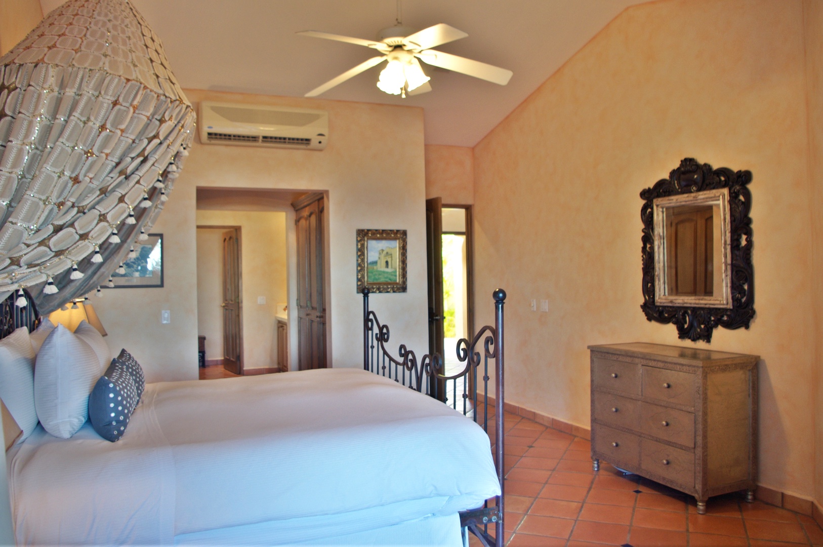 Step into your serene retreat with warm terracotta tiles and soft peach walls. Sink into plush linens beneath the gentle ceiling fan, surrounded by charming rustic touches and thoughtful climate control for your perfect night's rest.