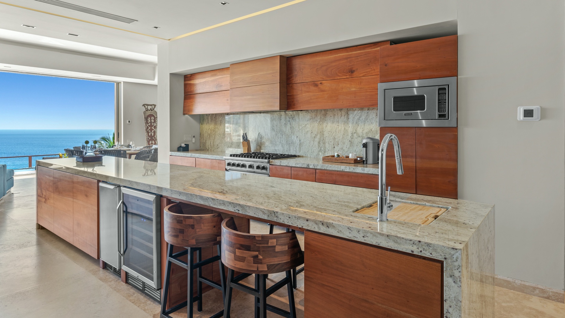 Your gourmet kitchen features warm wood cabinetry, granite countertops, and professional appliances, all opening to stunning ocean views. Gather at the island or step out to the terrace for seamless indoor-outdoor living.