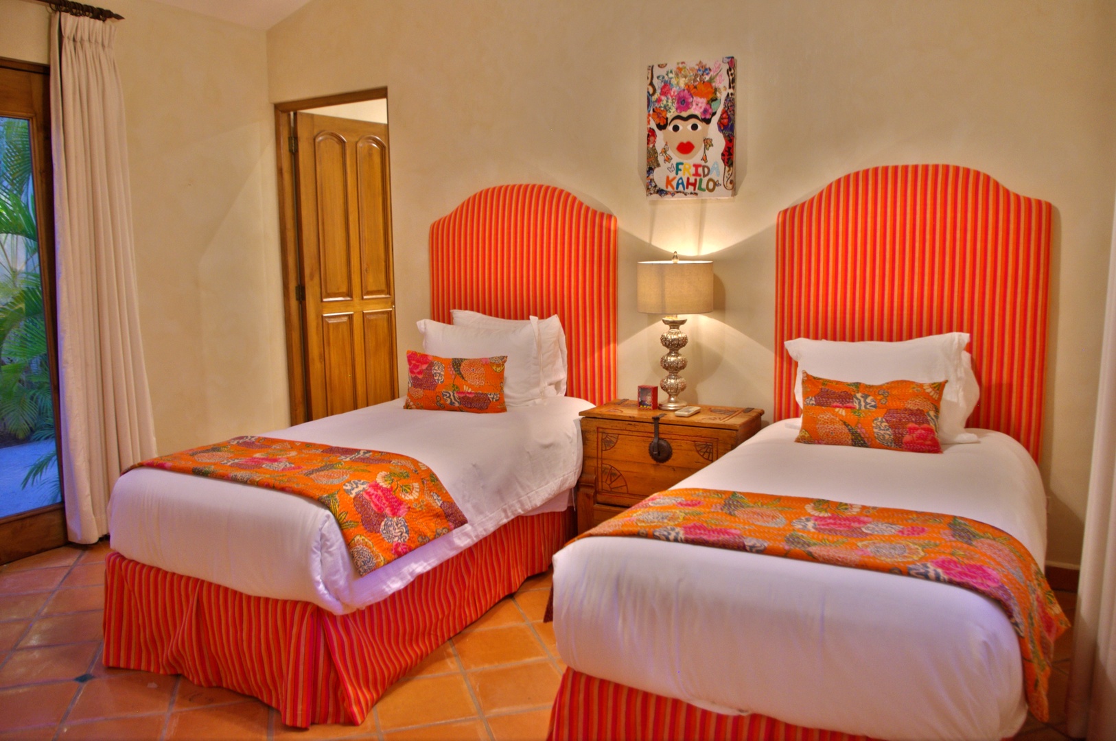 Two plush twin beds await your arrival, dressed in vibrant orange linens and colorful accent pillows. Warm terracotta floors and charming artwork add Mexican flair to your cozy retreat.