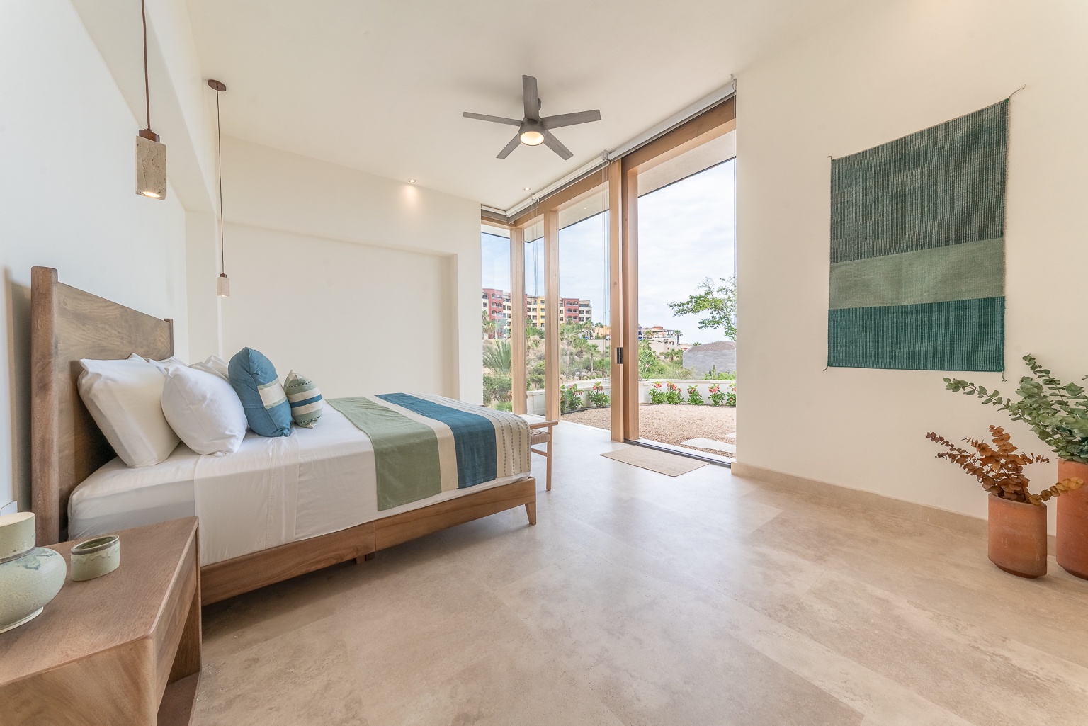 Your serene bedroom retreat features natural wood furnishings, soothing teal accents, and floor-to-ceiling windows that frame tranquil desert views. Drift off under the gentle ceiling fan, waking to warm sunlight and peaceful scenery.