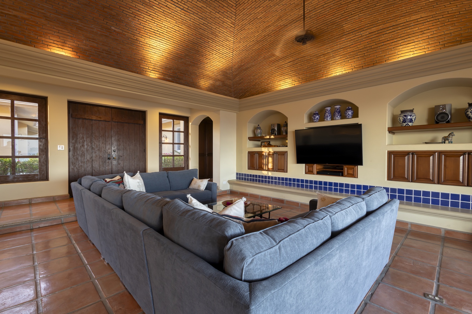 Unwind in this stunning living room featuring soaring brick ceilings, plush sectional seating, and authentic Mexican tilework that creates your perfect retreat.