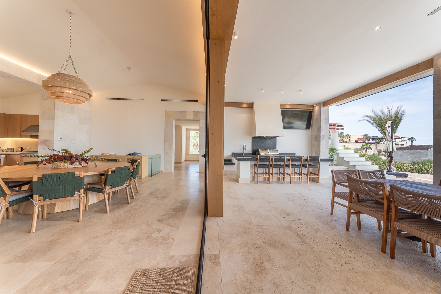 Bright, open-concept space where sunlit dining flows effortlessly into a modern kitchen. Palm trees frame the view, blending indoor elegance with breezy coastal ambiance perfect for gathering.