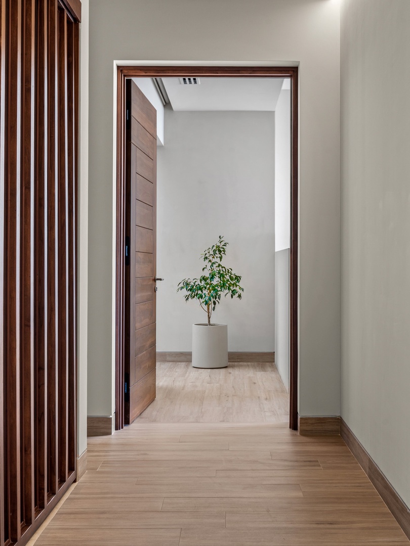 A warm wooden door frames the view into a minimalist hallway, where natural light filters softly from above, creating a serene and welcoming entryway.