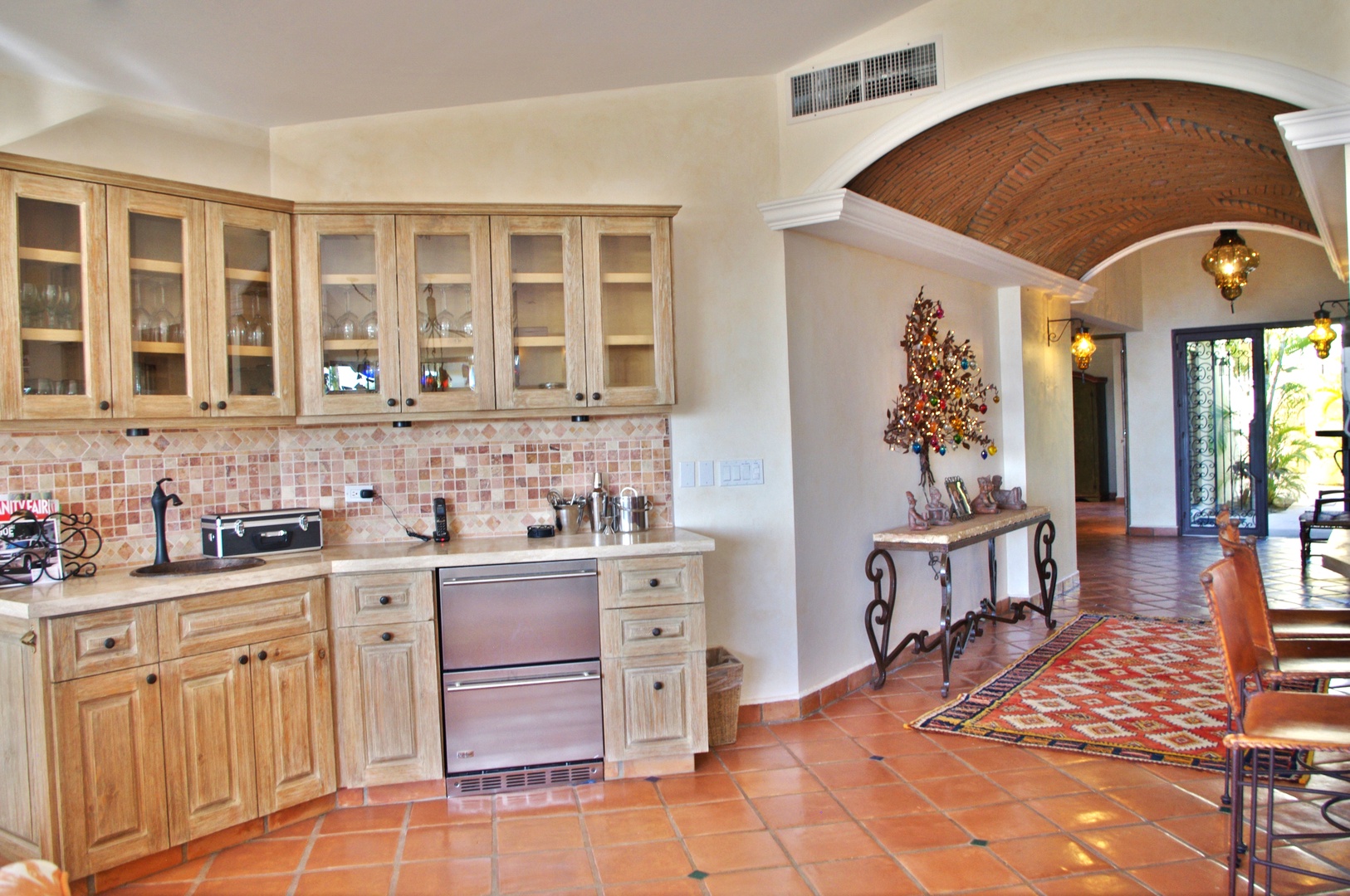 Spacious kitchen area with terracotta tile floors, natural wood cabinetry, and an elegant archway leading to sunlit living spaces—your home away from home.