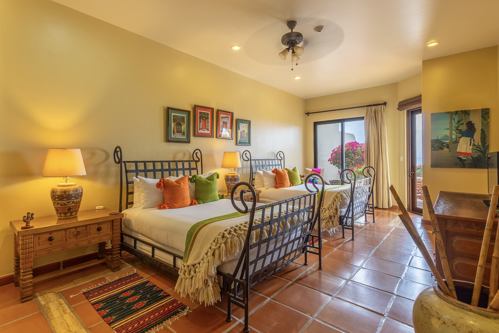 Your cheerful bedroom features twin beds dressed in crisp linens with vibrant accent pillows, inviting natural light, and direct access to your private terrace surrounded by blooming bougainvillea.