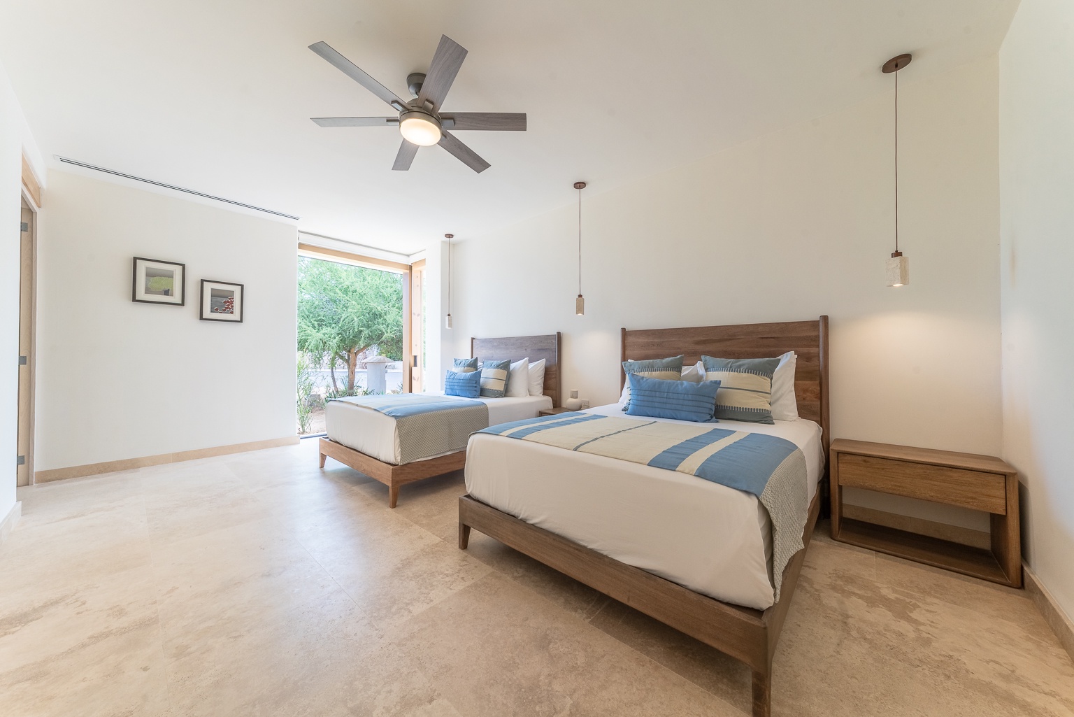 Drift off to sleep in this spacious bedroom where two plush beds await you beneath stylish pendant lighting and a gentle ceiling fan, while morning light filters through your window overlooking lush greenery.