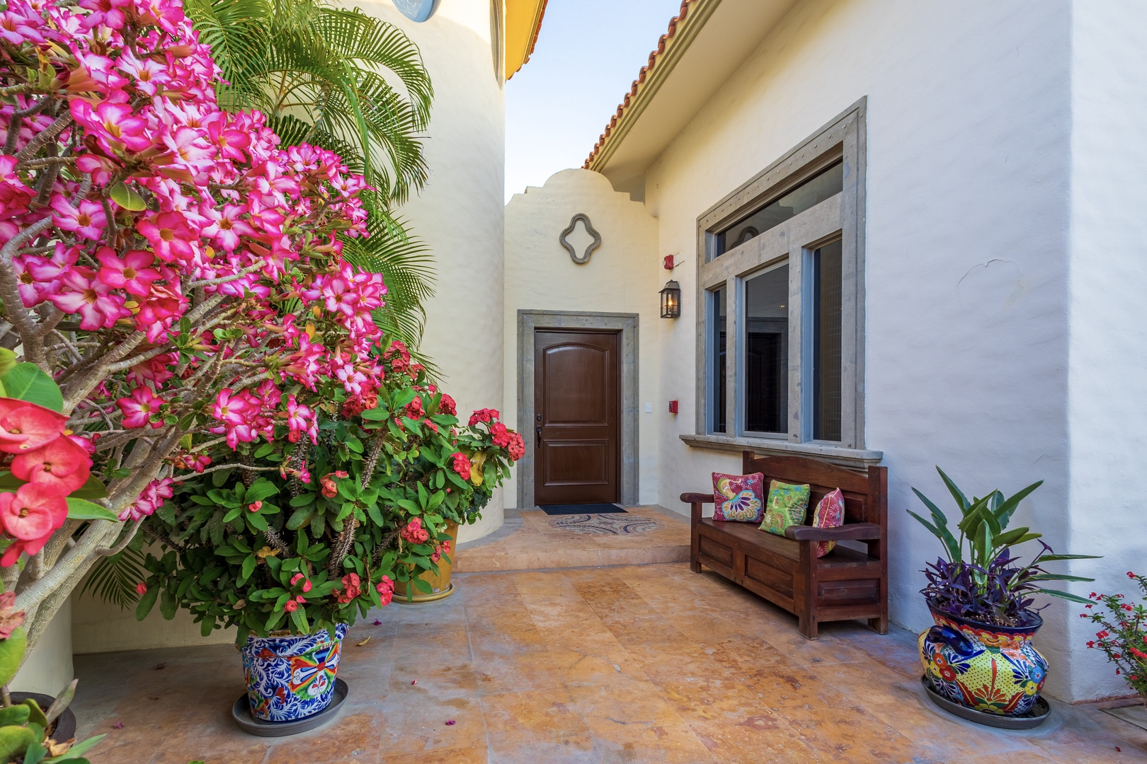 The entrance welcomes guests with vibrant blooms, a cozy wooden bench, and warm architectural details perfect for a peaceful arrival moment.
