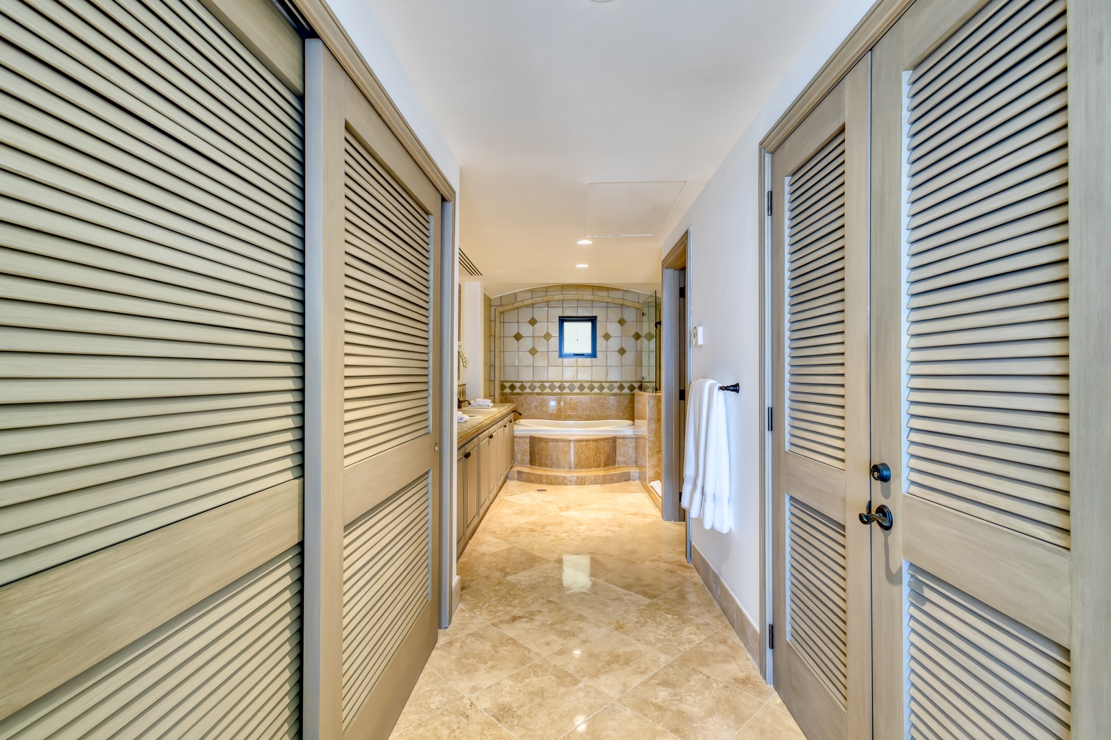Step into your private spa-like retreat. Louvered doors open to reveal a luxurious bath framed by warm tile and soft lighting, creating your personal haven for relaxation.