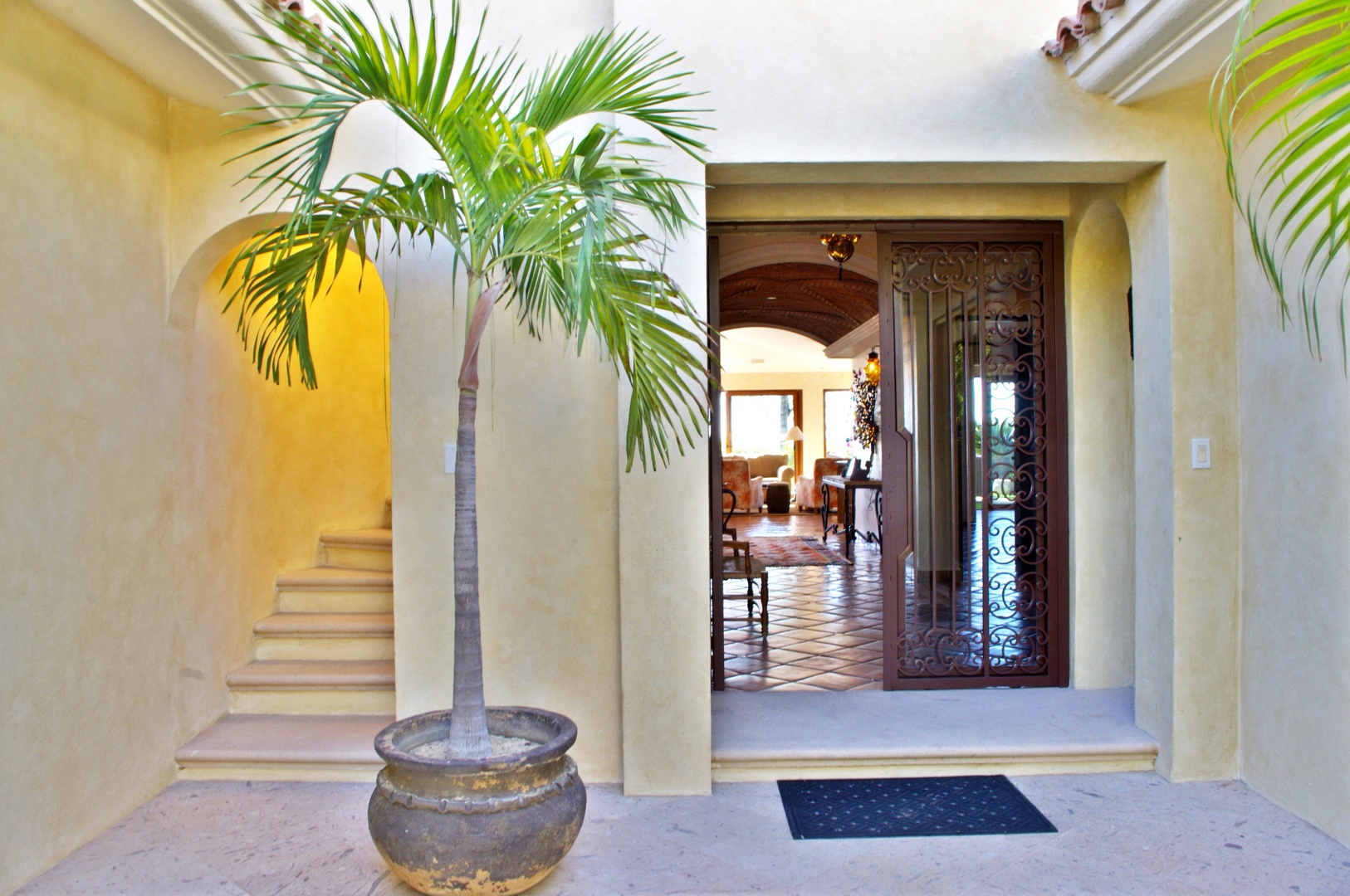 This grand entrance welcomes you with warm terracotta tile flooring, an ornate carved wooden door, and a tropical palm tree that sets a tranquil, resort-style tone for your stay.