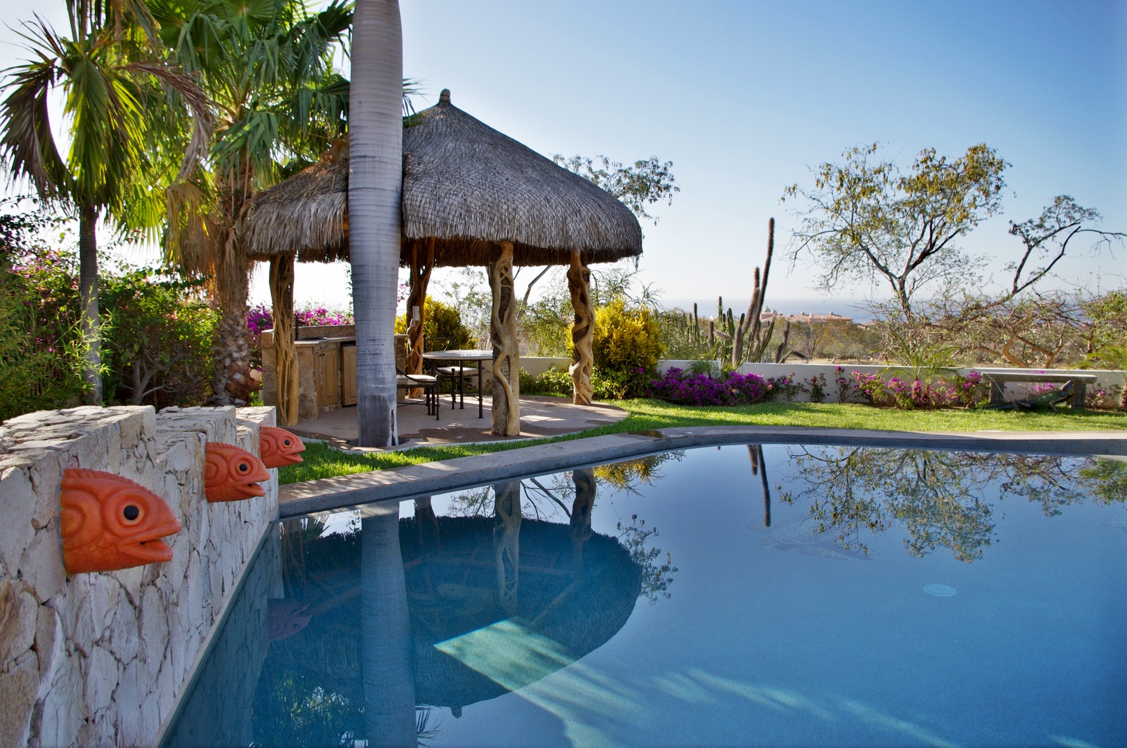 Private pool oasis with thatched palapa, lush tropical gardens, and mountain vistas—your serene desert escape awaits.