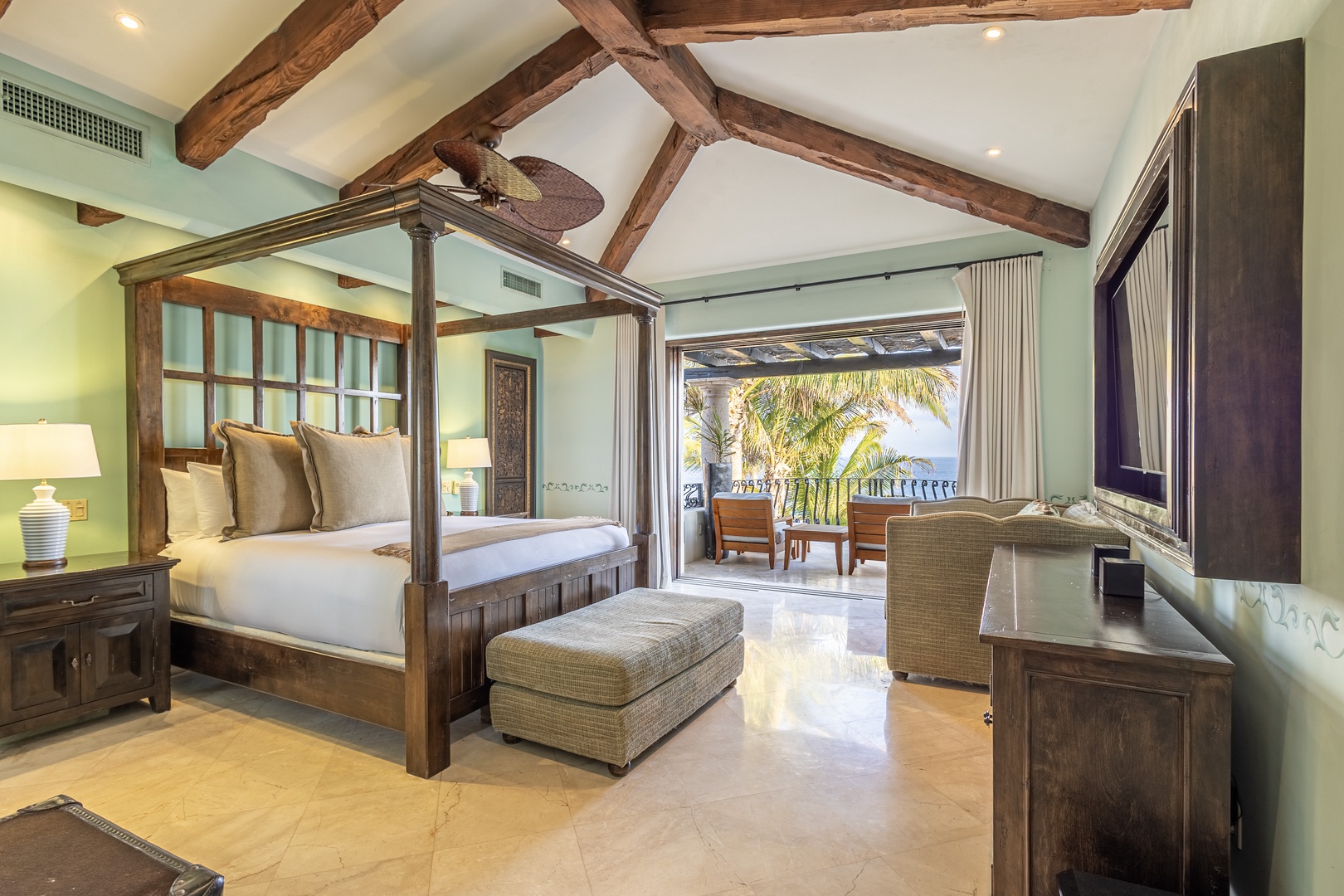 Unwind in your airy retreat with rustic beams overhead, a plush four-poster bed, and balcony doors opening to lush palm views and coastal vistas.