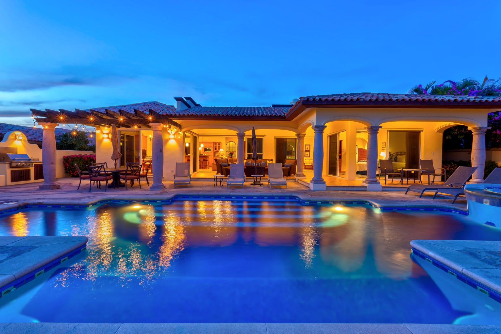 Luxurious villa showcases Mediterranean architecture with illuminated pool area and elegant outdoor entertaining spaces during twilight hours.