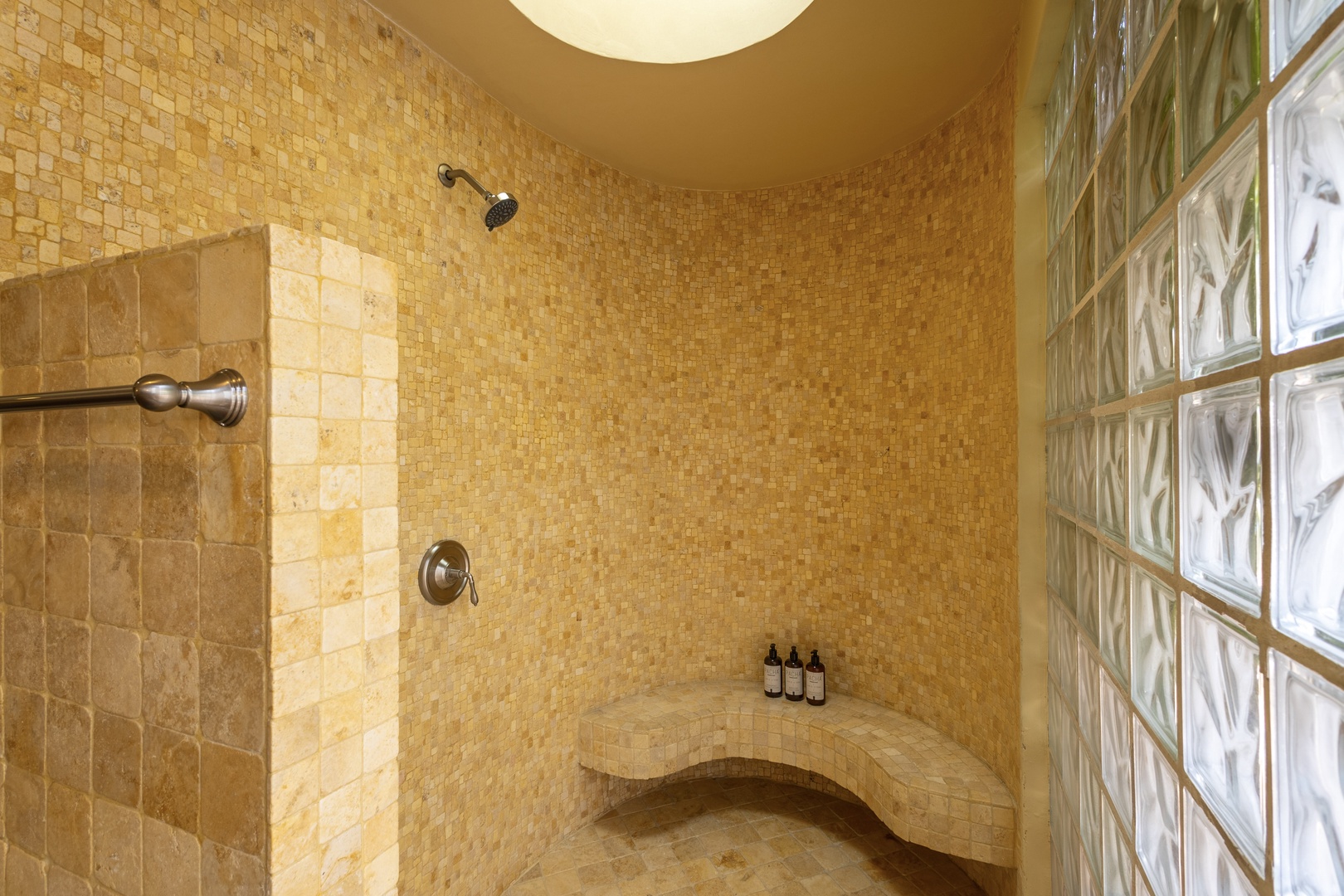 Unwind in your luxurious walk-in shower with elegant mosaic tiling, curved bench seating, and a glass block wall that fills the space with natural light.