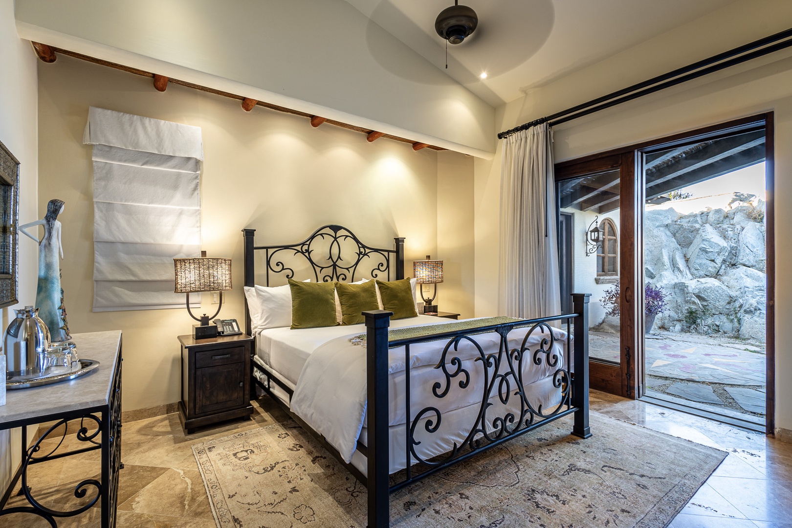 Step into your serene bedroom retreat with a plush bed, elegant iron detailing, and direct access to your private courtyard oasis through beautiful French doors.