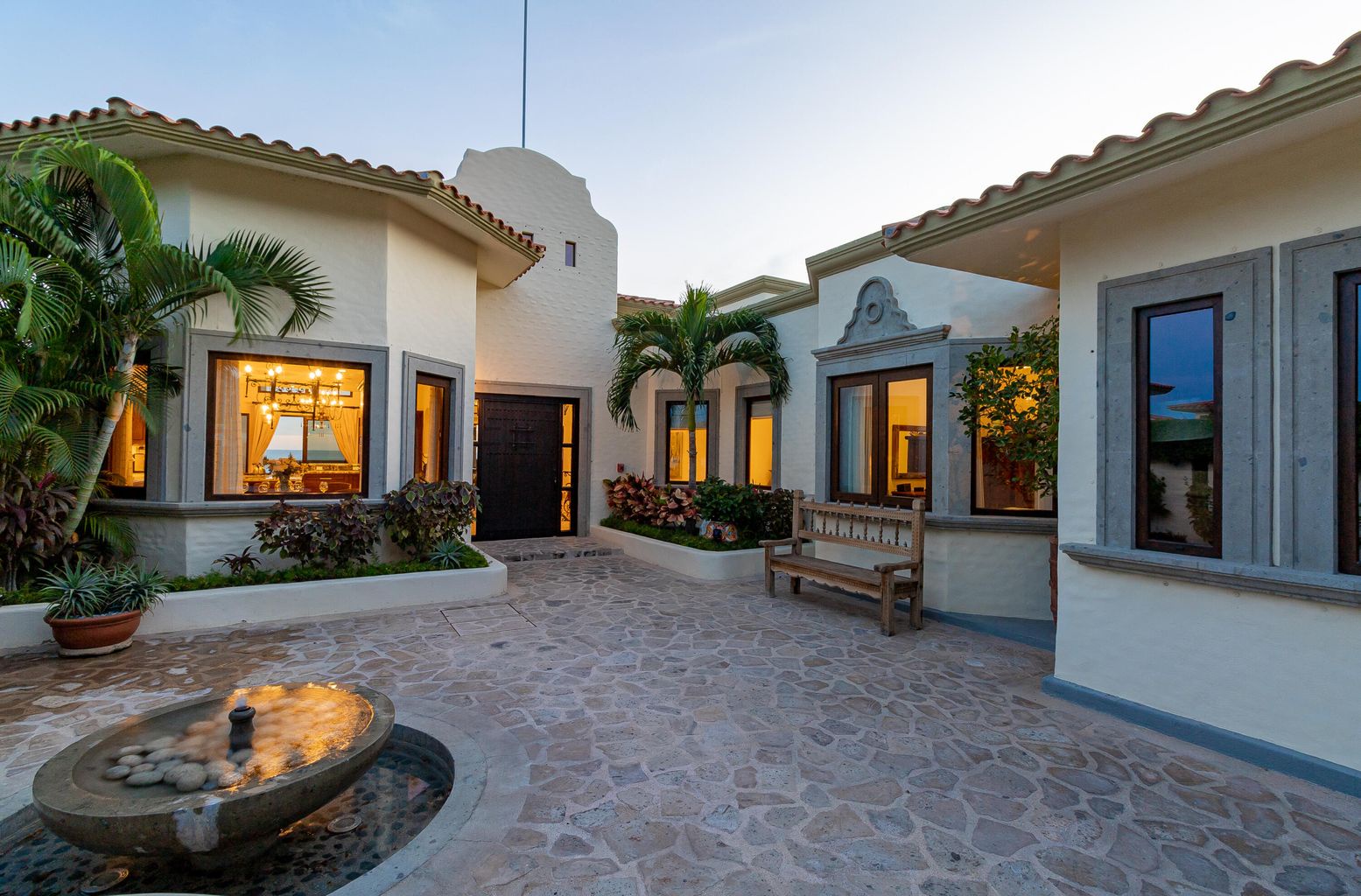 A charming Spanish-style courtyard welcomes you with warm lighting, lush tropical palms, and a soothing stone fountain—your peaceful retreat after a day of adventure.