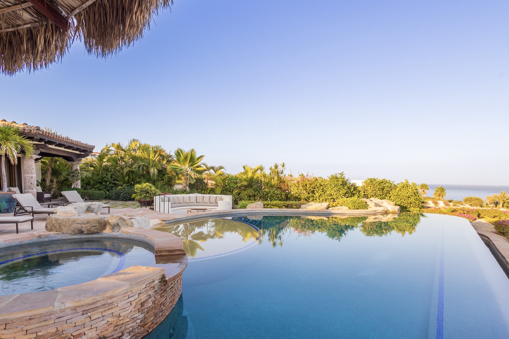This luxurious beachfront property features an infinity pool and hot tub overlooking the ocean, surrounded by tropical gardens and thatch-roof palapas for ultimate seaside relaxation.
