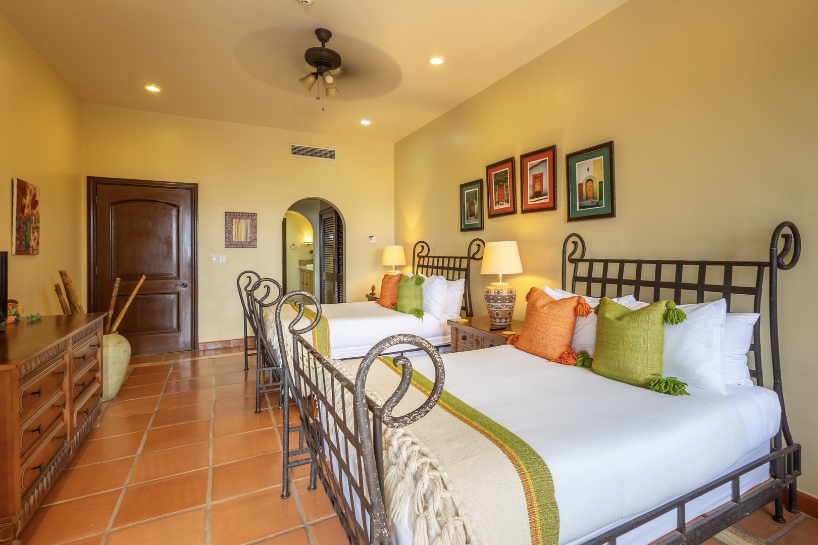 Unwind in your inviting guest room with twin beds dressed in crisp linens and colorful accent pillows. The space features warm tile floors, artwork, and a ceiling fan to keep you comfortable.