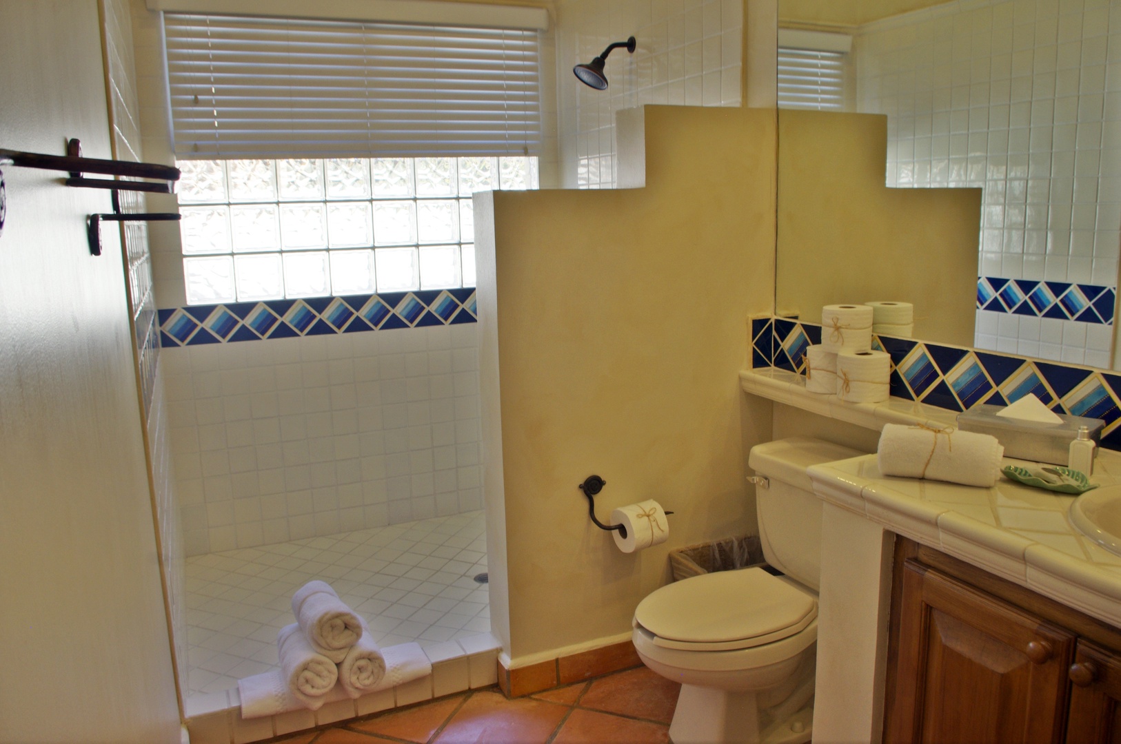 Step into this bright, tiled bathroom with a spacious walk-in shower, colorful mosaic accents, and fresh towels waiting for you. Natural light fills the room through the windows.