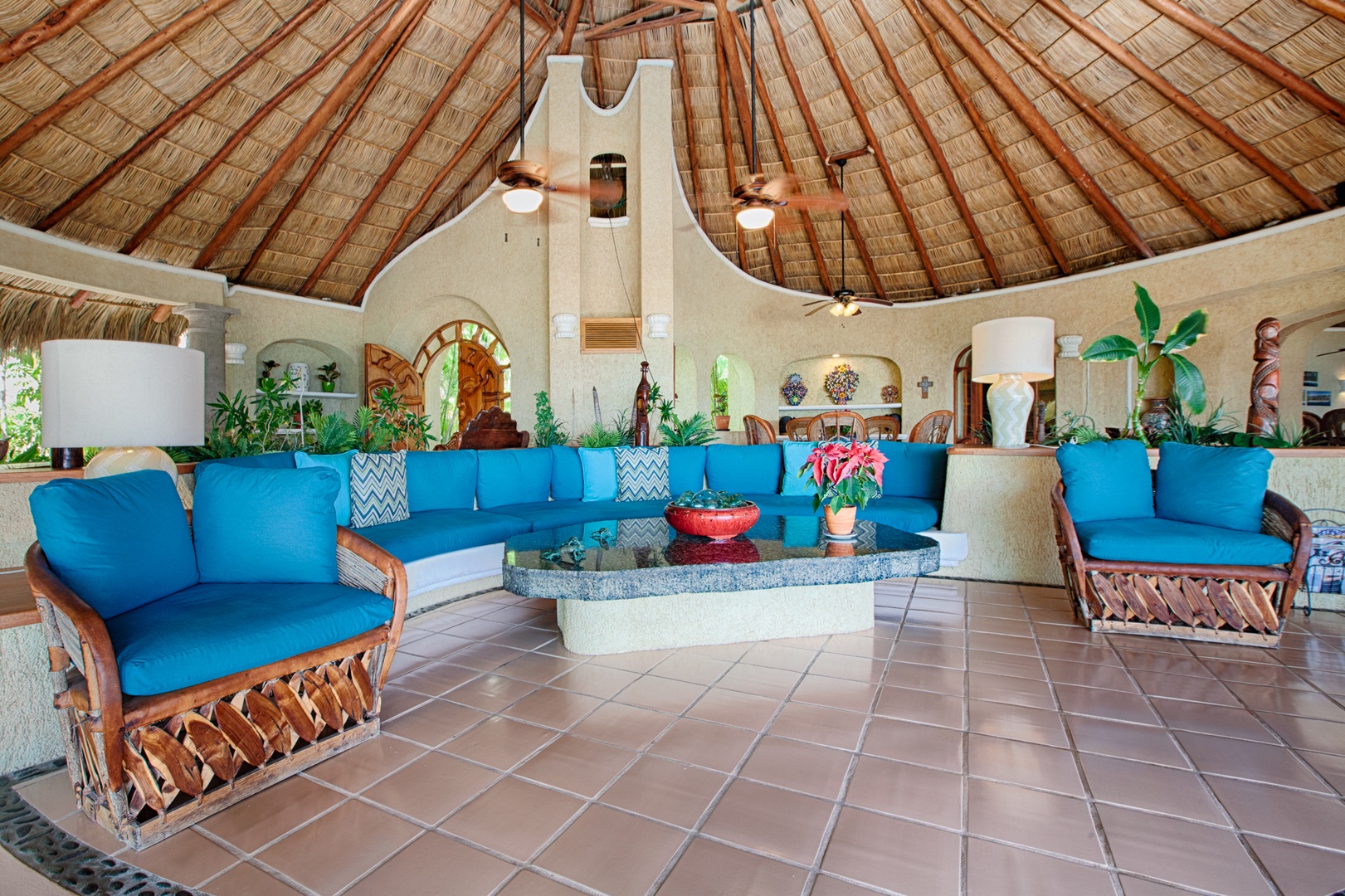 Relax in this stunning palapa lounge with vibrant blue seating, natural thatched ceiling, and tropical décor creating your perfect island retreat.