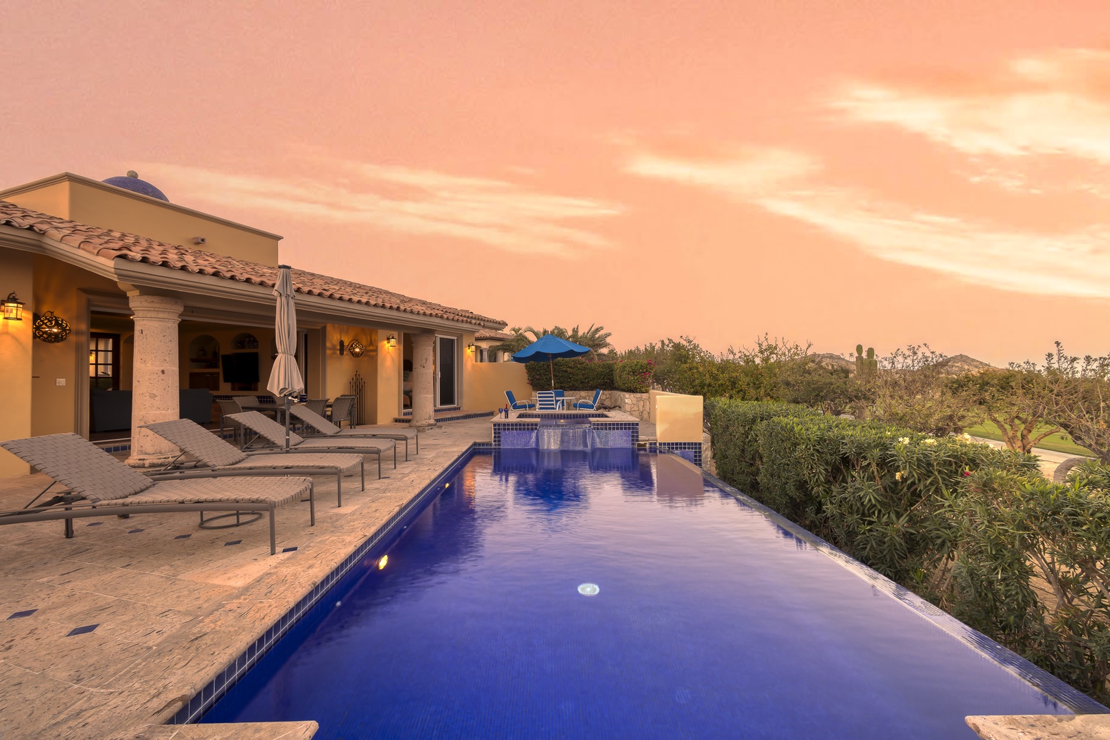 A stunning desert retreat featuring a sparkling infinity pool and dramatic sunset sky over the property.