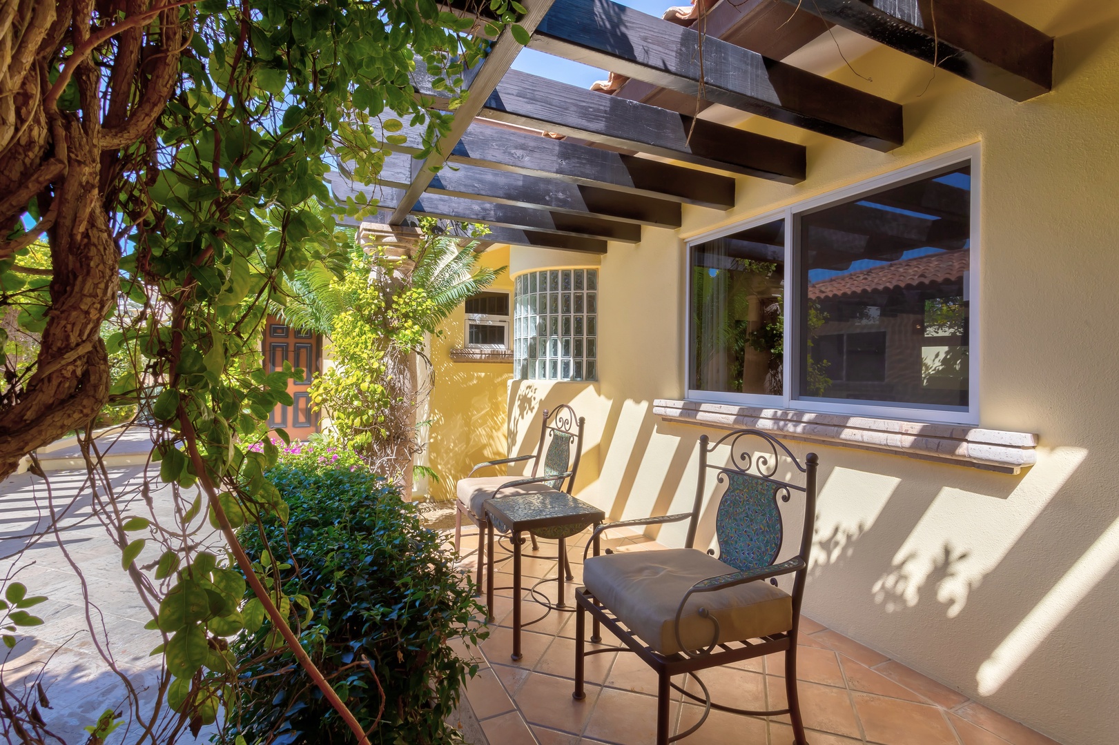 Relax in your private covered terrace with garden views and dappled sunlight filtering through the pergola overhead.