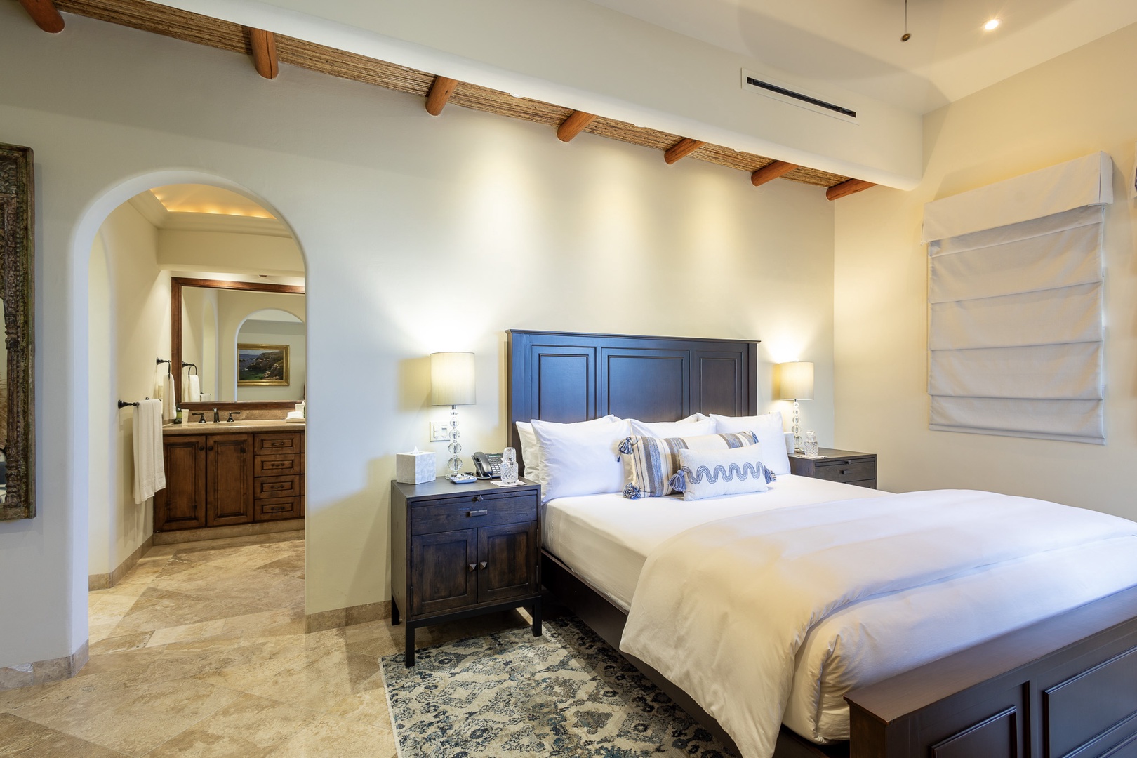Sink into luxurious comfort in your private bedroom, where elegant wood furnishings and soft linens invite deep rest. The arched doorway leads to your ensuite bath, blending rustic charm with modern ease.