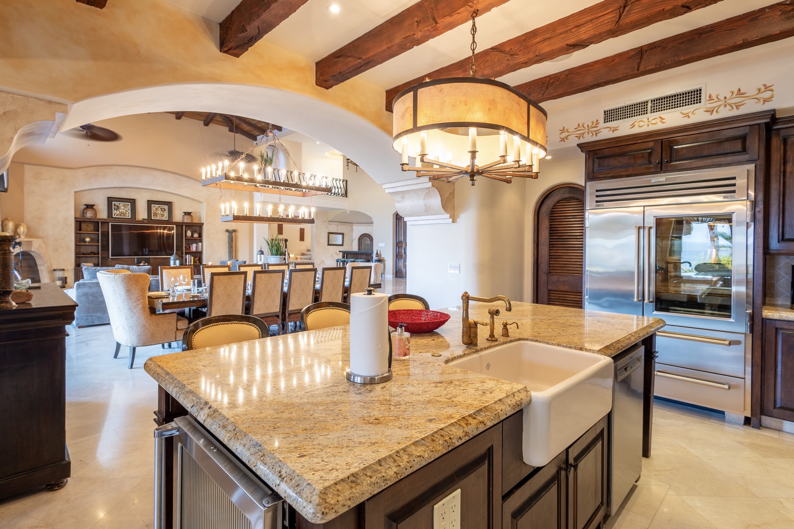 Gather around the spacious kitchen island to prepare meals together, bathed in warm light from handcrafted chandeliers and rustic wooden beams overhead.