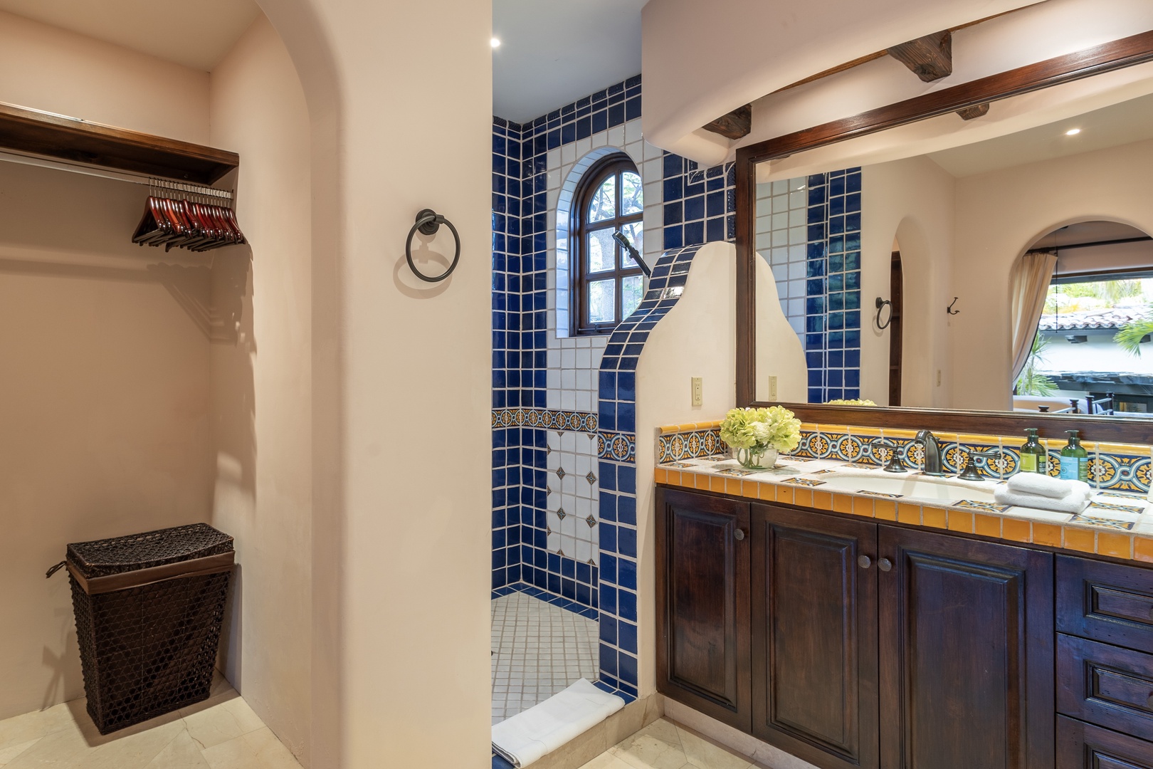 Step into your beautifully tiled bathroom where vibrant blue mosaic and hand-painted accents create a charming Mediterranean atmosphere. Fresh flowers and warm wood cabinetry invite you to relax and refresh.
