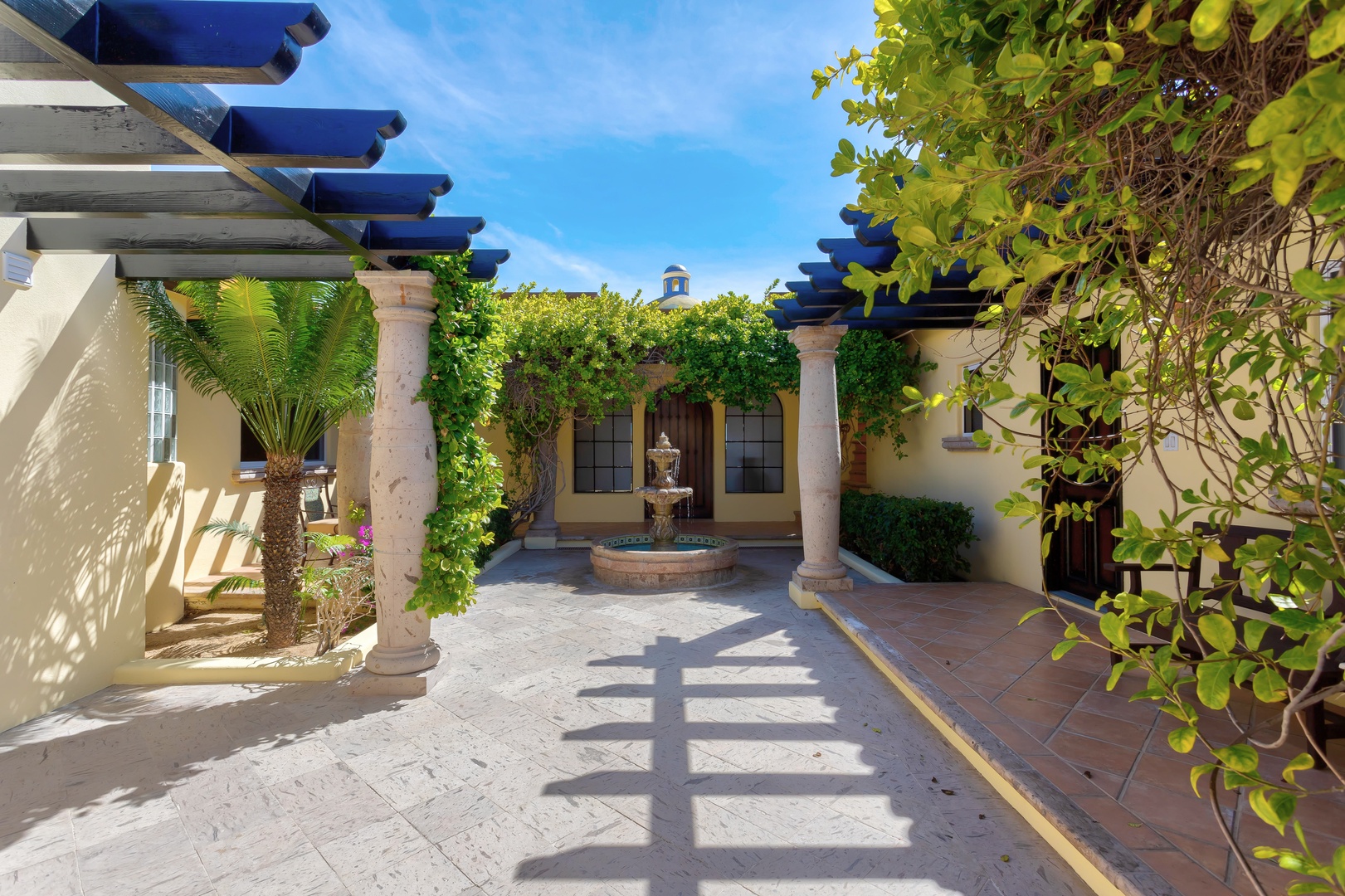 A Mediterranean-style courtyard with classic columns, vine-covered pergola, and central fountain creates an elegant outdoor retreat.