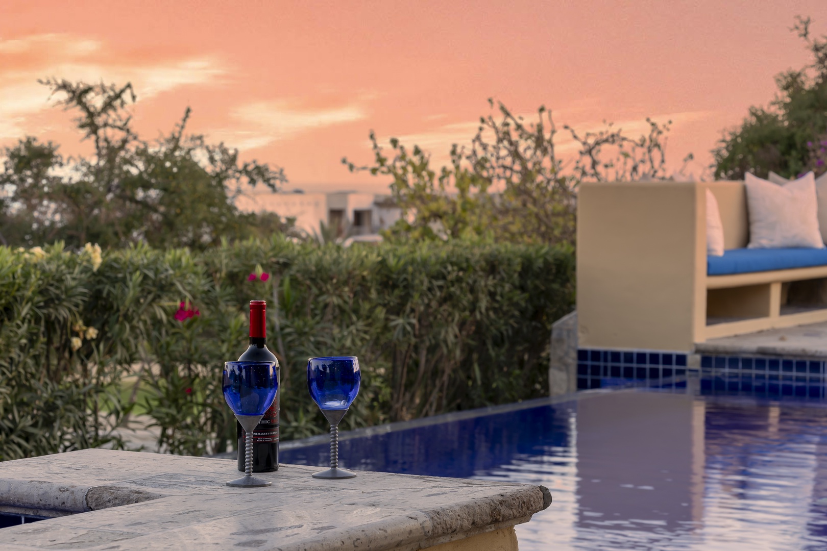 Stunning sunset paints the sky as evening settles over this serene poolside retreat with lush gardens.
