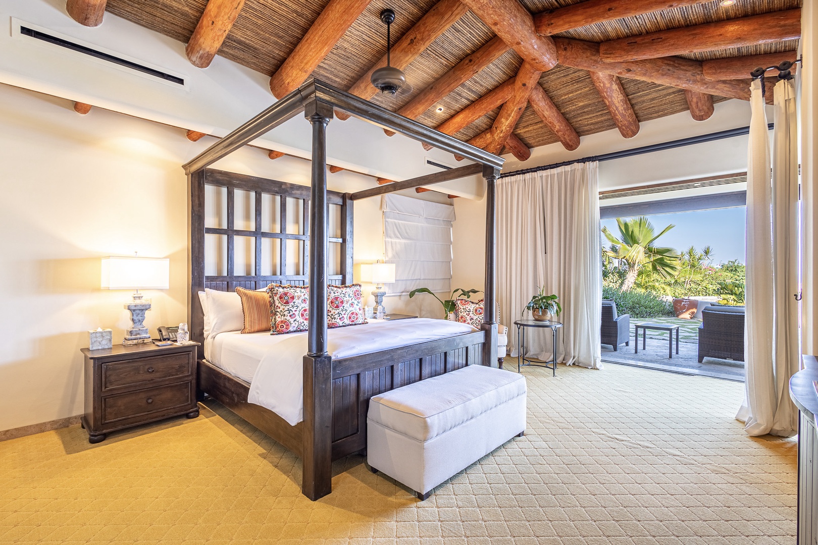 Picture yourself waking up in this serene bedroom, where rustic beams and a canopy bed meet modern comfort. Step through flowing curtains onto your private terrace with stunning garden views.