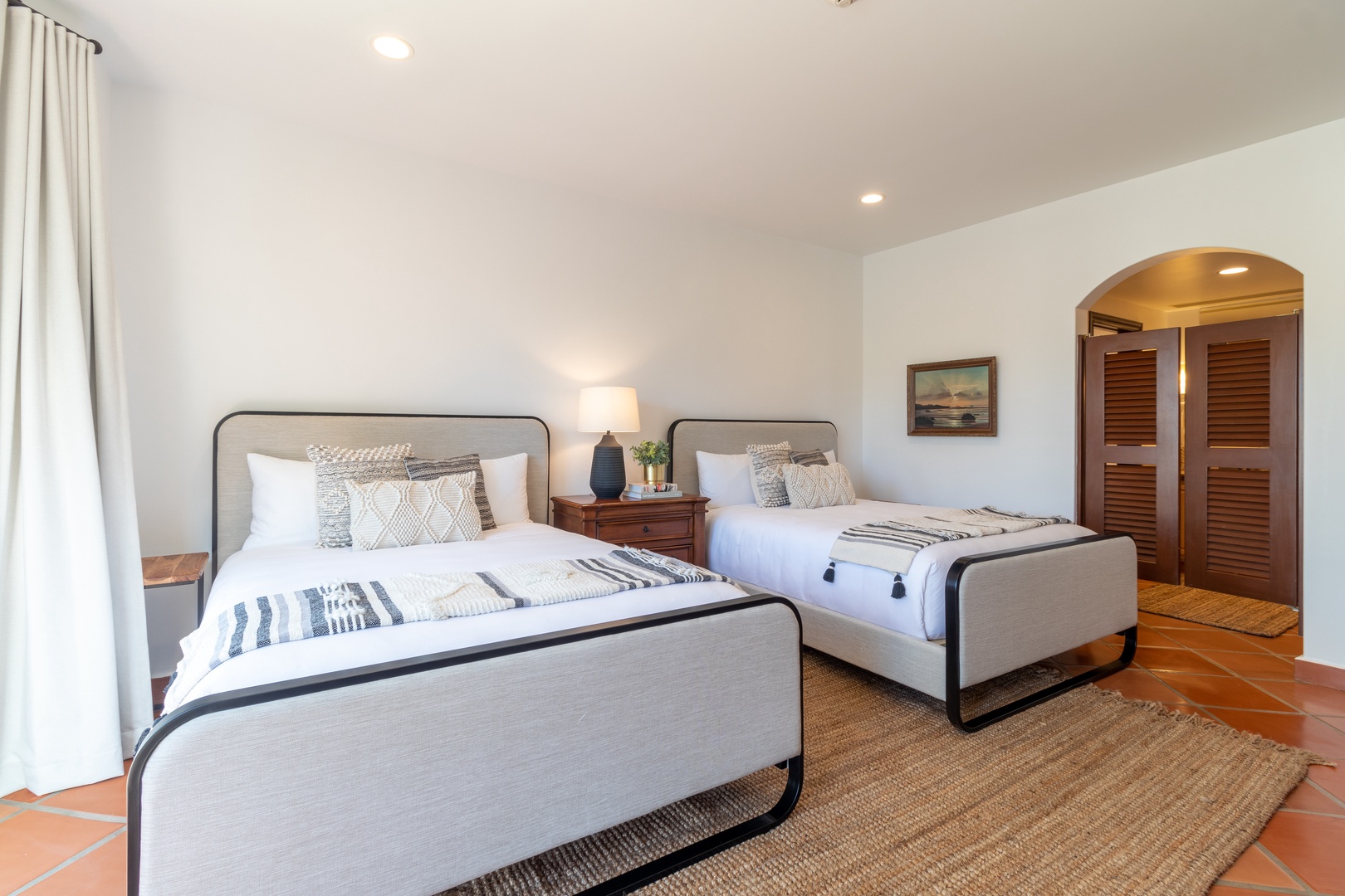 Relax in this bright, airy bedroom with two plush beds, charming terracotta floors, and warm wood accents that create a cozy coastal retreat for your stay.