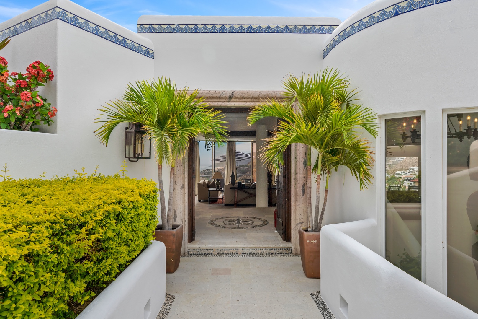 Modern white villa with blue tile accents, tropical palms, and colorful blooms creates an elegant arrival experience.