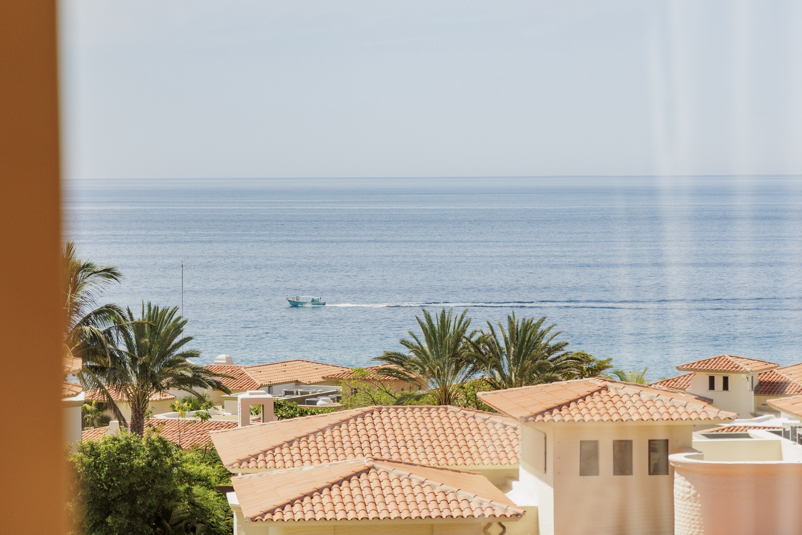 Panoramic sea view from this coastal property, featuring tile-roofed villas framed by swaying palms and calm blue waters stretching to the horizon.