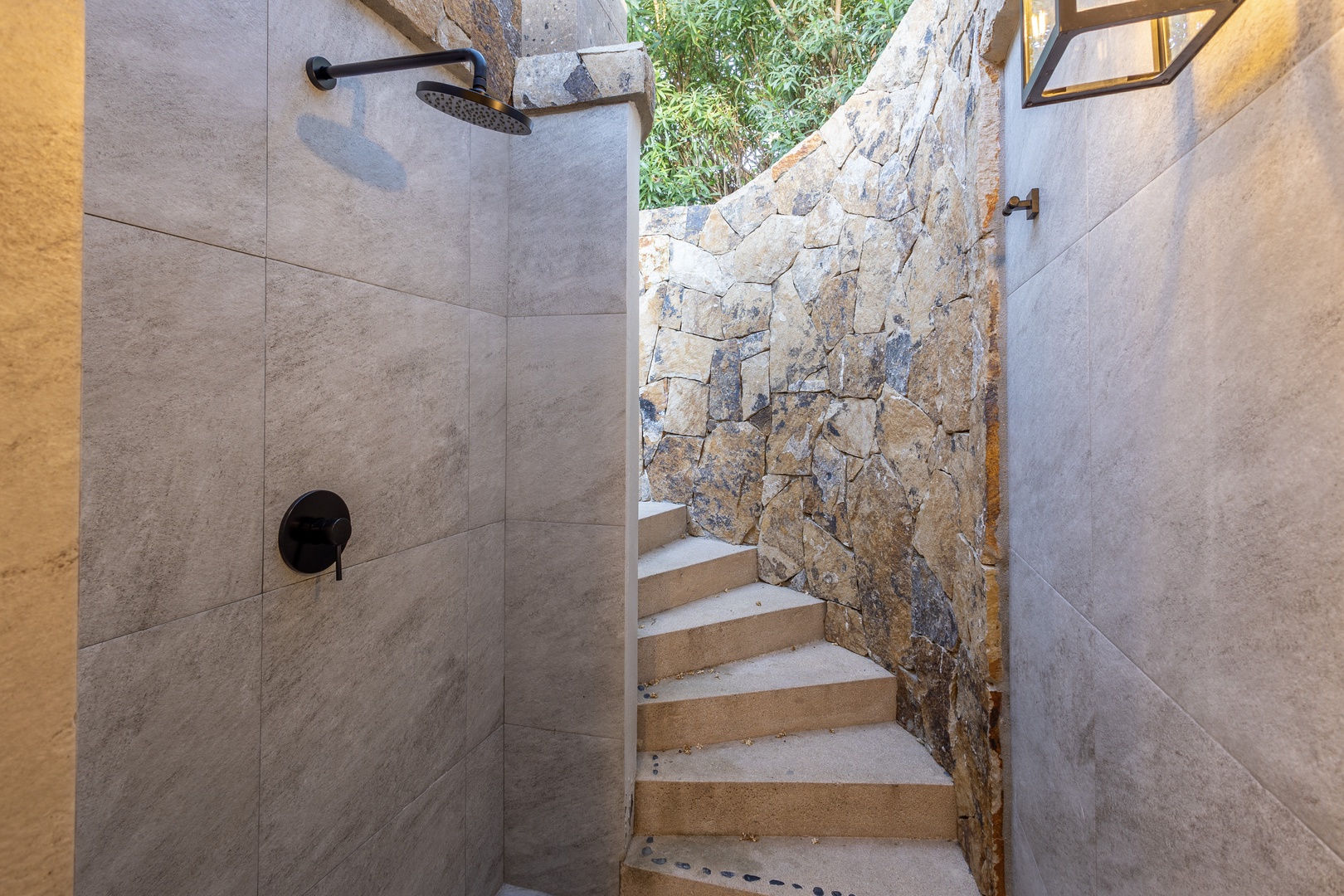 An open-air shower blends stone walls with tropical greenery above, creating a private retreat where nature meets modern comfort.