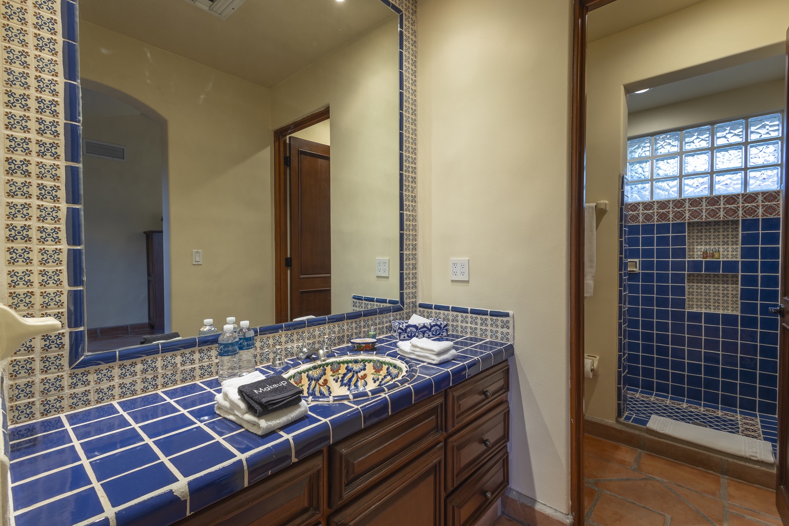Unwind in your beautiful bathroom featuring handcrafted Mexican tiles, rich wood vanities, and a spacious walk-in shower with stunning blue ceramic details.
