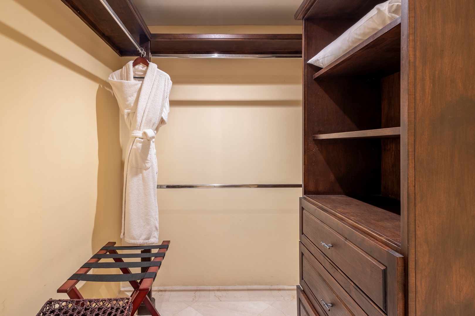 Your spacious walk-in closet features rich wood shelving and ample hanging space, with a plush robe awaiting your arrival and room for all your belongings.