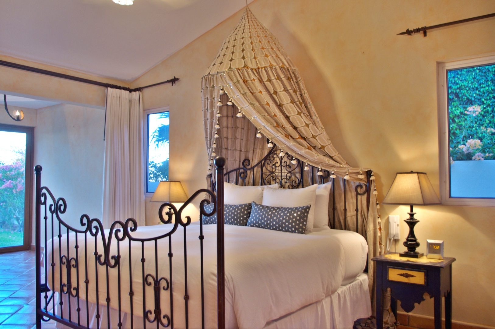 Drift off under a romantic canopy draped over an elegant wrought-iron bed, with garden views framing your peaceful retreat.
