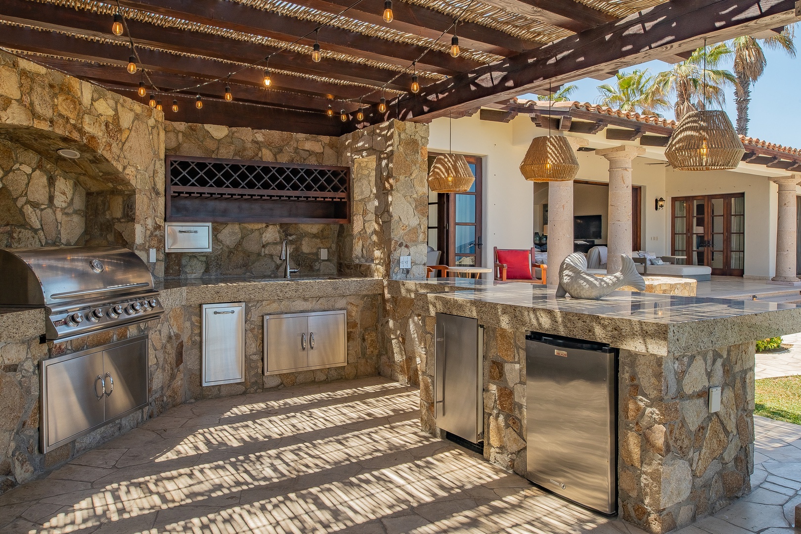 Your stunning outdoor kitchen awaits with stone countertops, professional grill, and tropical ambiance under twinkling lights.