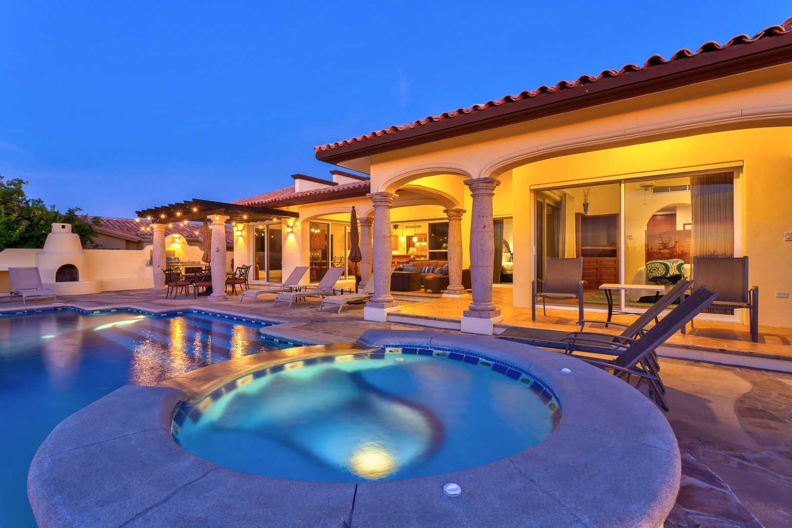 Luxurious villa with illuminated pool and spa at twilight, showcasing elegant Mediterranean architecture and outdoor entertaining spaces.