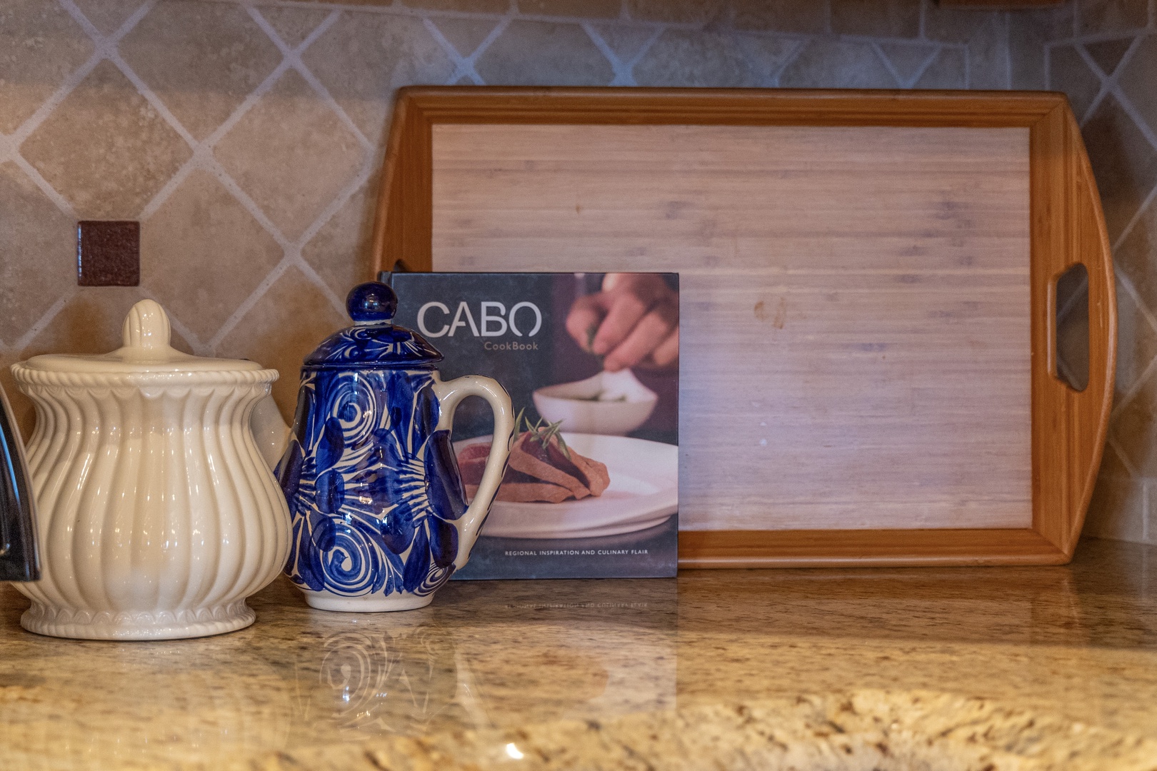 A welcoming countertop setup features a wooden serving tray, decorative teapots, and a local Cabo cookbook—your invitation to explore regional flavors and cozy moments during your stay.