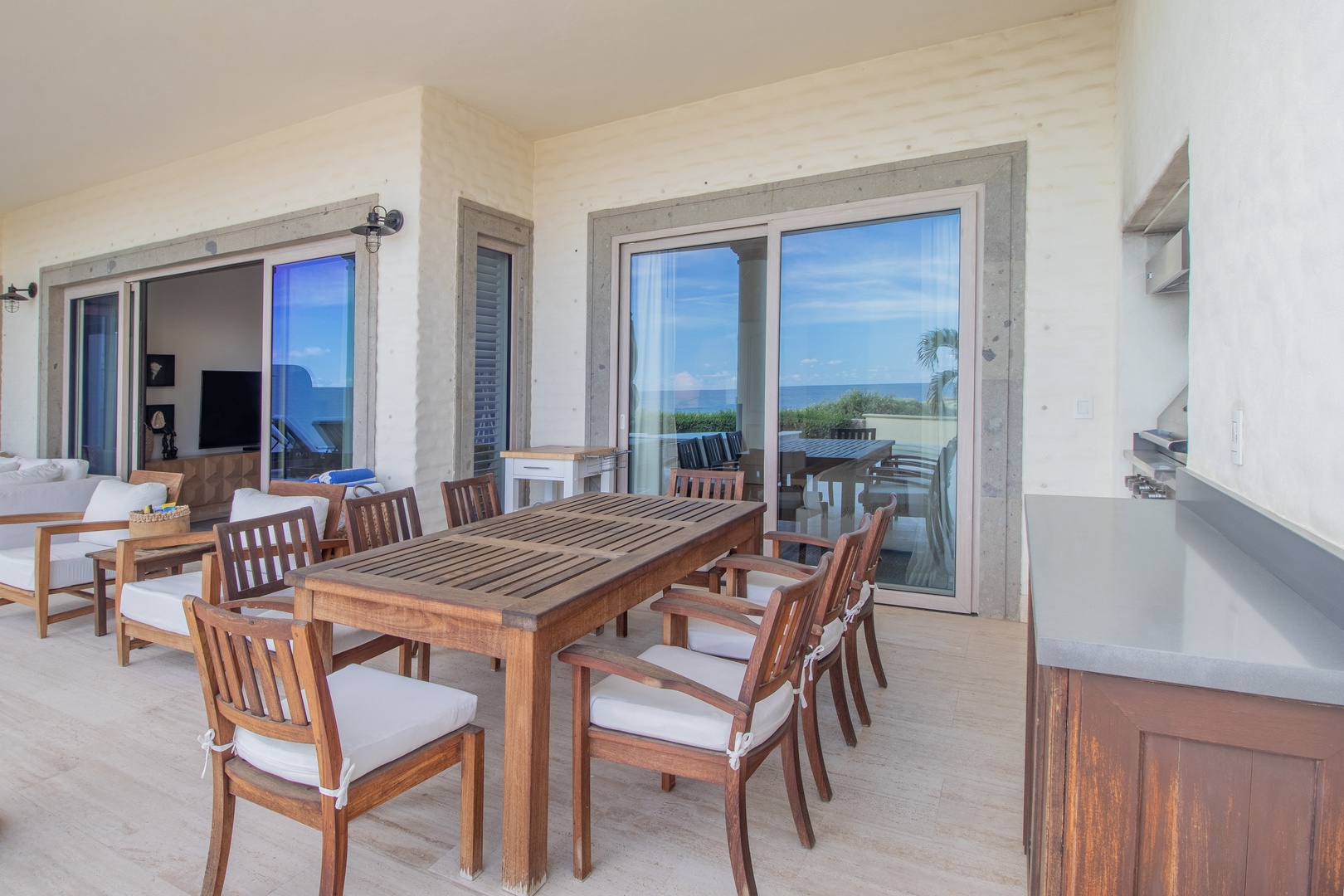 Your covered terrace awaits with a large dining table and coastal views framed by glass doors—perfect for gathering with loved ones over leisurely meals in the fresh ocean breeze.