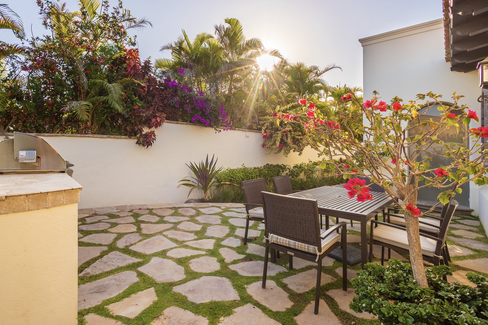 Gather around your private outdoor dining area surrounded by vibrant tropical blooms, lush palms, and cascading bougainvillea catching the warm golden sunlight—a serene spot for unforgettable meals.