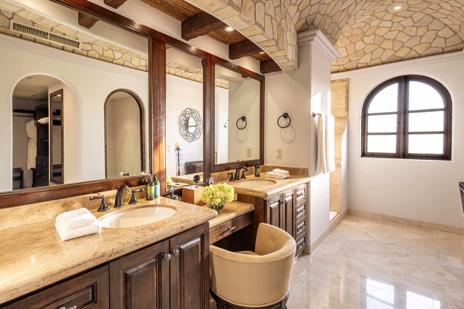 Your spacious bathroom blends rustic elegance with modern comfort—dual vanities, warm wood accents, stone archways, and soft natural light create a luxurious retreat for your morning routine.