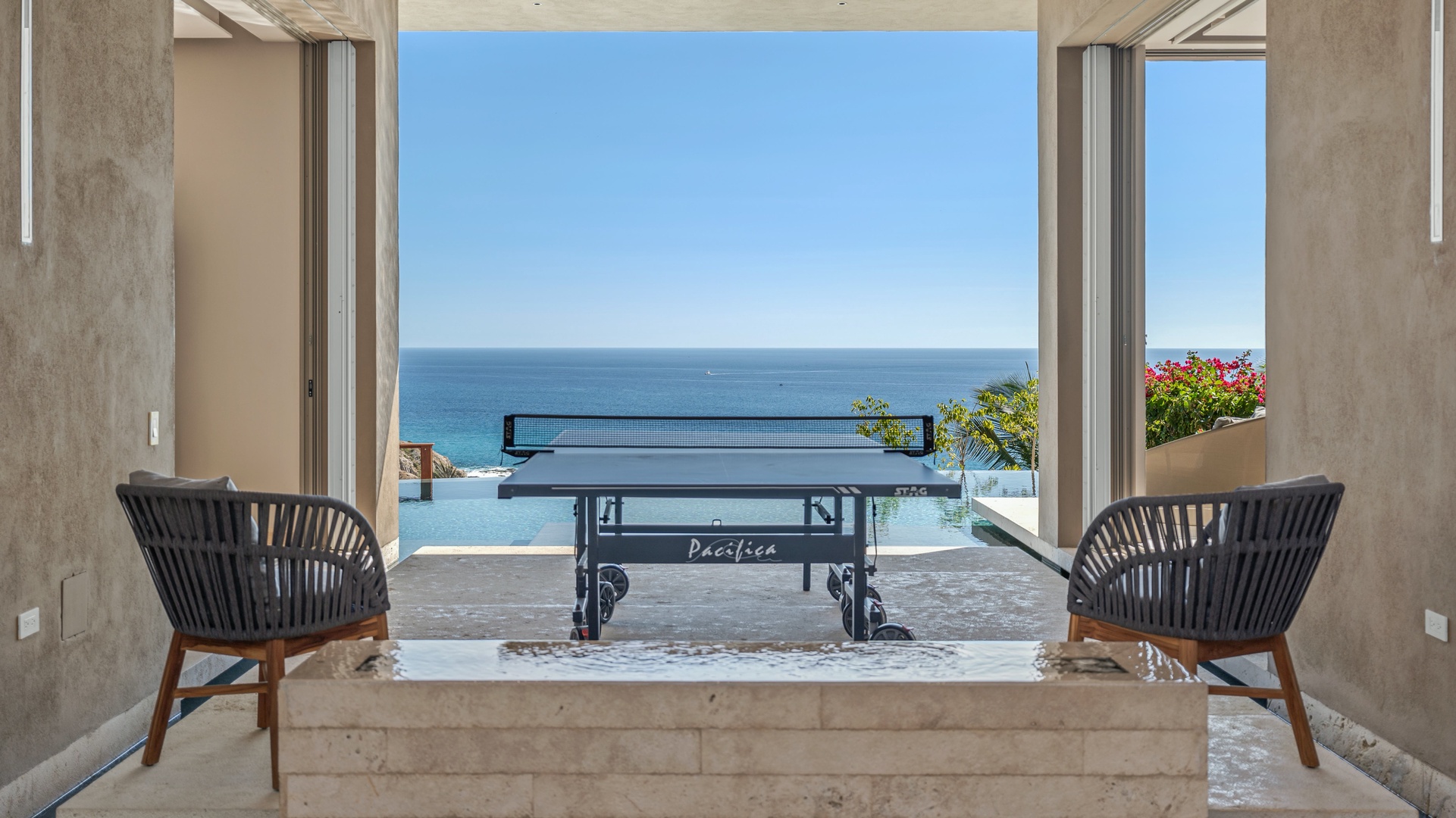 Step through open doors to discover a tranquil game room where ping pong awaits, framed by breathtaking ocean vistas and your own private infinity pool beyond.
