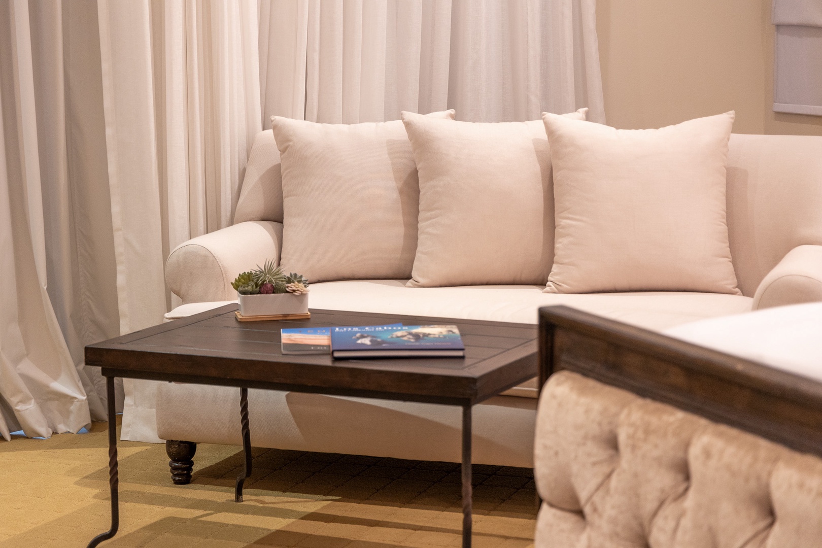 Settle into this soothing neutral living room with plush cushions and thoughtful touches, including fresh reading material and a succulent. Your peaceful retreat awaits.