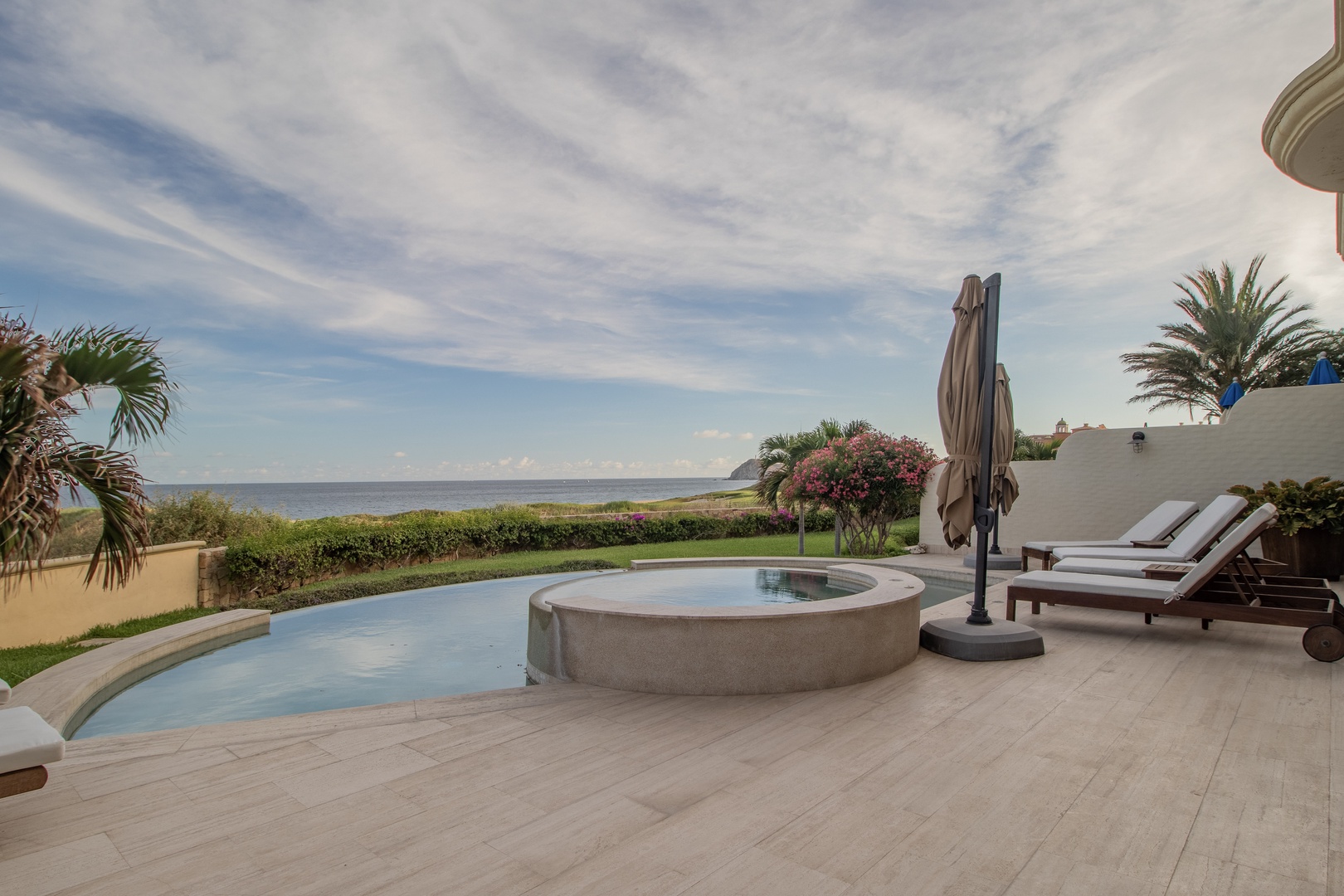 Your private pool and hot tub overlook lush gardens and the sparkling sea beyond, inviting you to unwind under endless blue skies.